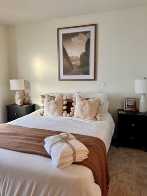 A neatly made bed with a brown blanket, white pillows, and a framed picture on the wall.