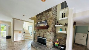 A spacious living room with a stone fireplace, a staircase leading to another level, and a view of greenery outside. - LUXURIOUS VILLA WATERFRONT NEAR SIESTA KEY BEACH (Sarasota)