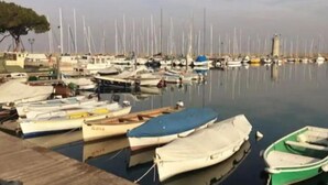 A marina with various boats docked, a wooden pier, and a distant tower. - Stay overnight in a luxurious apartment, central location within walking distance of the lake (Desenzano del Garda)