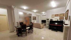 A living room with a dining table, chairs, a sofa, a piano, and a television. - Stay overnight in a luxurious apartment, central location within walking distance of the lake (Desenzano del Garda)