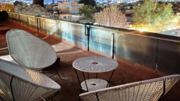 A rooftop terrace with two wicker chairs and a small round table, overlooking a cityscape at night. - Casa Paty! (Oaxaca de Juárez)