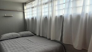 A bedroom with a bed, curtains, and a wall-mounted shelf. - Casa Paty! (Oaxaca de Juárez)