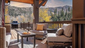 A covered outdoor deck with wicker furniture, a table with fruit and wine glasses, and a grill.