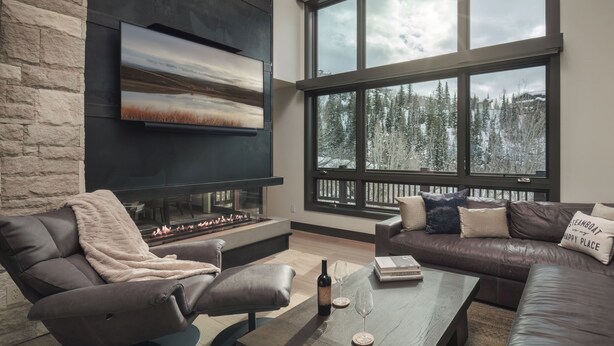 A modern living room with a fireplace, leather sofas, and a large window with a snowy view.