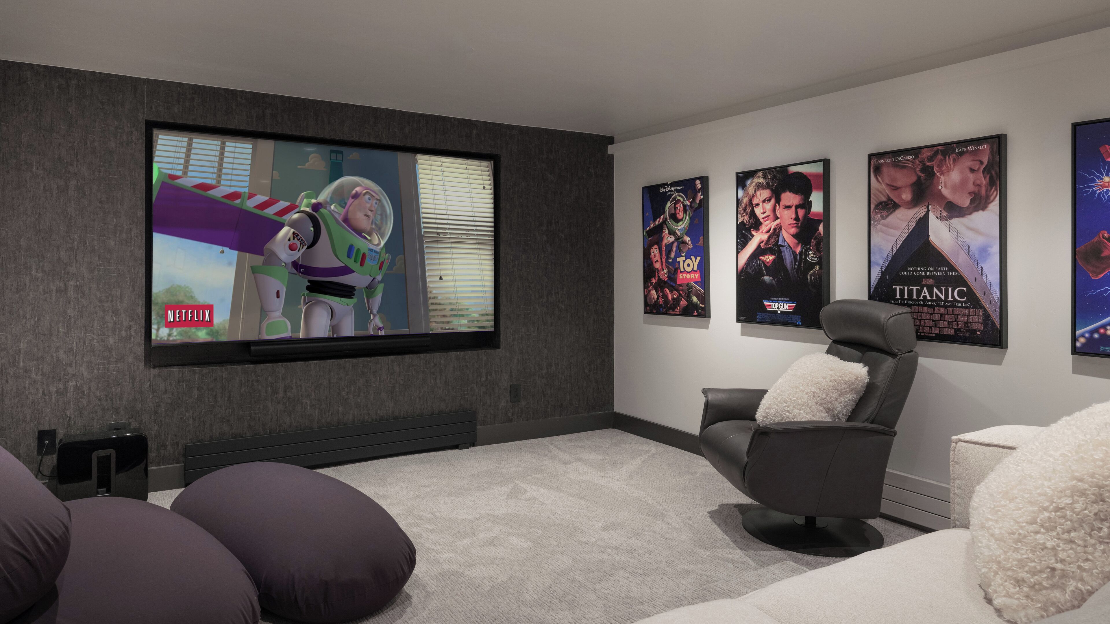 Une salle de cinéma privée équipée d’un grand téléviseur à écran plat, d’un fauteuil inclinable et de plusieurs affiches de films accrochées au mur.