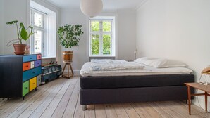 A bedroom with a bed, a dresser with colorful drawers, a potted plant, and a window with a view of greenery.