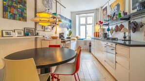 A modern kitchen with white cabinets, a black countertop, and red chairs. There are various kitchen appliances and a window providing natural light.