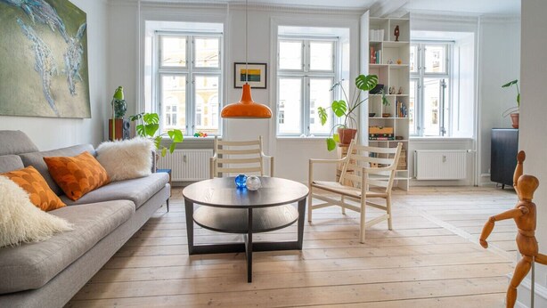 A spacious living room with a grey sofa, wooden chairs, a round coffee table, and a bookshelf.