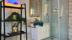 A modern bathroom with a glass shower enclosure, a neon massage sign, and a minimalist sink area.