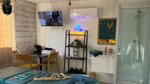 A massage room with a massage table, a TV, a shelf with massage tools, and a shower area.