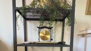 A black metal shelf unit with a decorative plant on top, a golden object in the middle, and a black object on the bottom shelf.