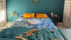 A bedroom with teal patterned wallpaper, a bed with a leaf-patterned duvet, and various wellness items on the bed.