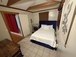 Un dormitorio con una cama, una mesita de noche, un aparador y una puerta que da a otra habitación.