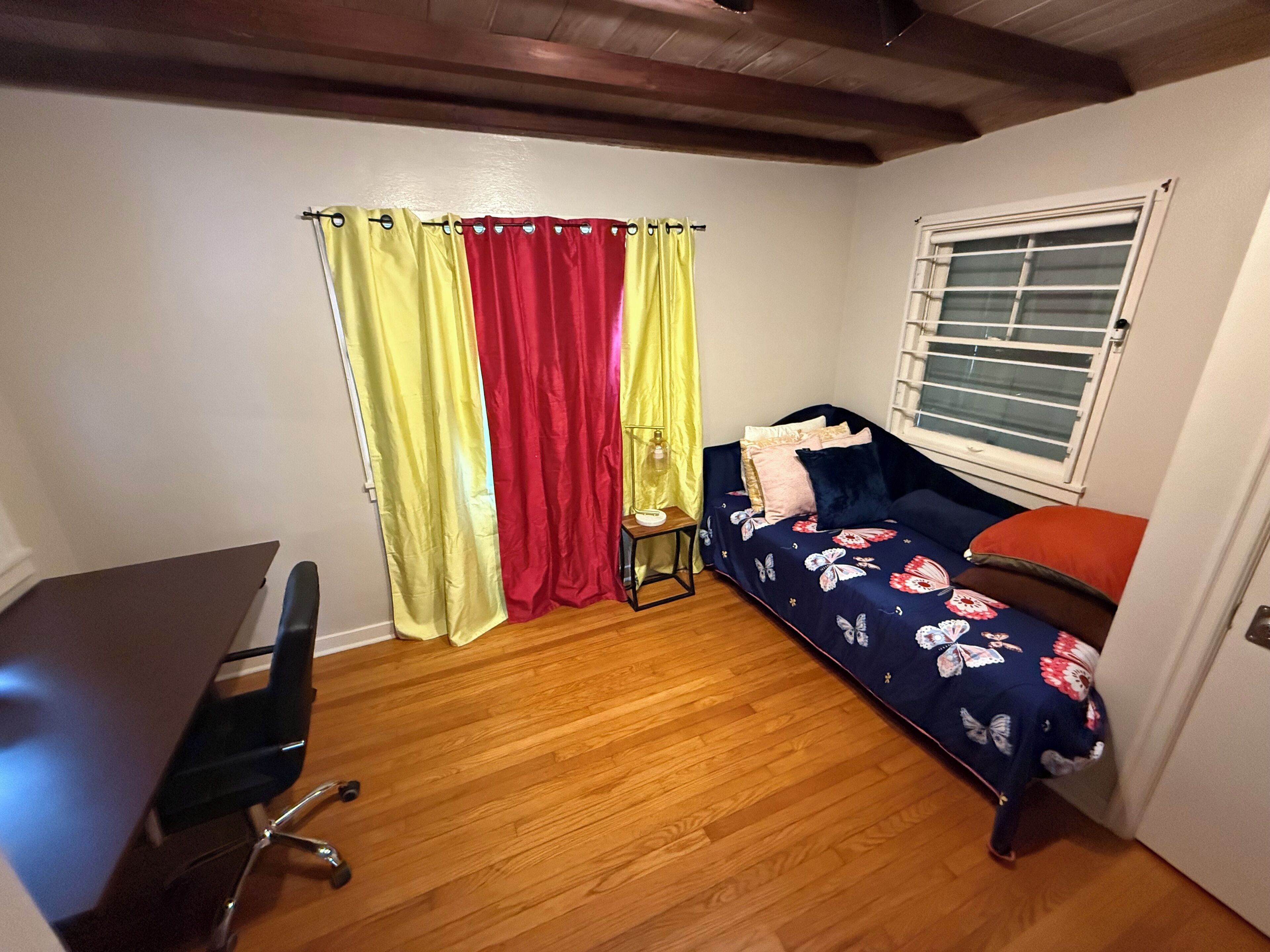 A small room with a bed, a desk, and a window with blinds.