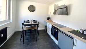 Cozinha moderna com mesa de jantar posta para dois, coifa de aço inoxidável e janela que permite entrada de luz natural.