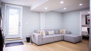 A modern living room with a grey sectional sofa, a small round table, and a door leading to a balcony. - Cozy and Private Basement apartment / Ideal for Relaxation or Work (Brampton)