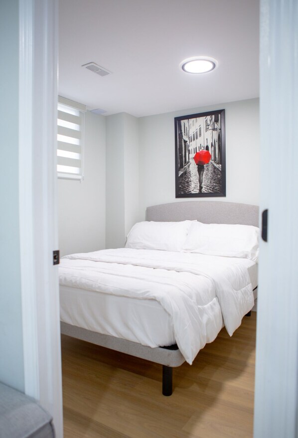 A bedroom with a bed, white bedding, a ceiling light, a window with blinds, and a framed picture on the wall. - Cozy and Private Basement apartment / Ideal for Relaxation or Work (Brampton)