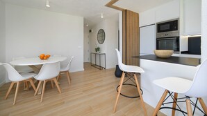Cozinha moderna com armários brancos, micro-ondas e forno. Possui uma área de refeições com mesa e cadeiras brancas.