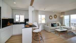 Um apartamento moderno com cozinha, sala de jantar e sala de estar. Possui uma janela ampla com vista, um sofá e uma mesa de centro.