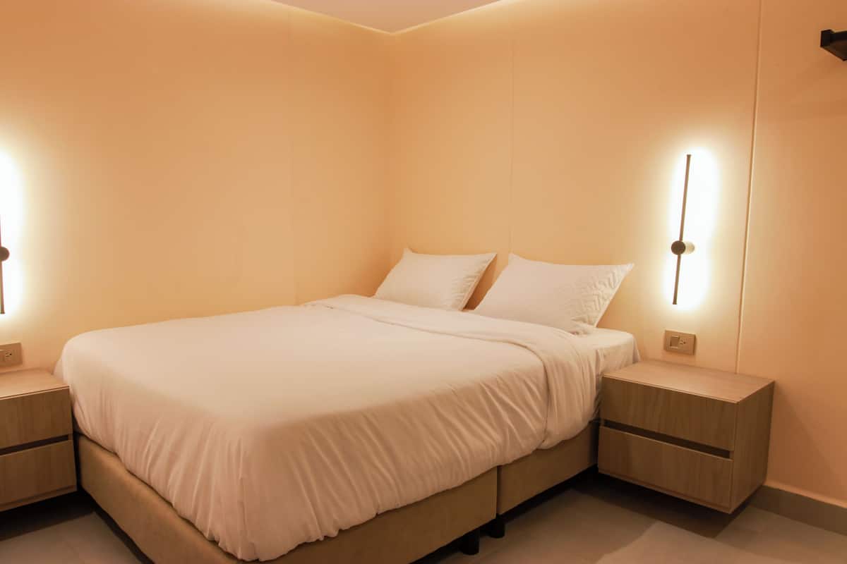 A neatly made bed with white linens in a modern bedroom with built-in nightstands and wall-mounted lighting.