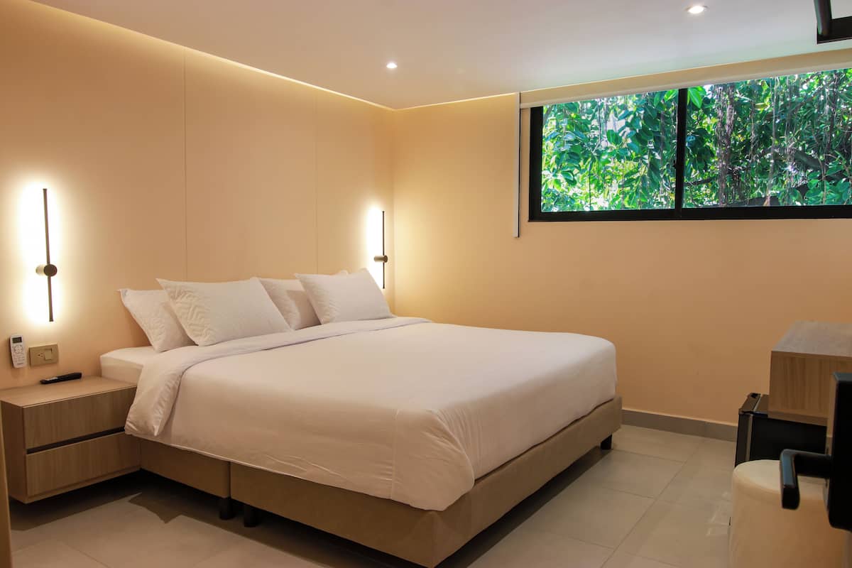 A modern bedroom with a large bed, bedside tables, a desk, and a window with a view of greenery.