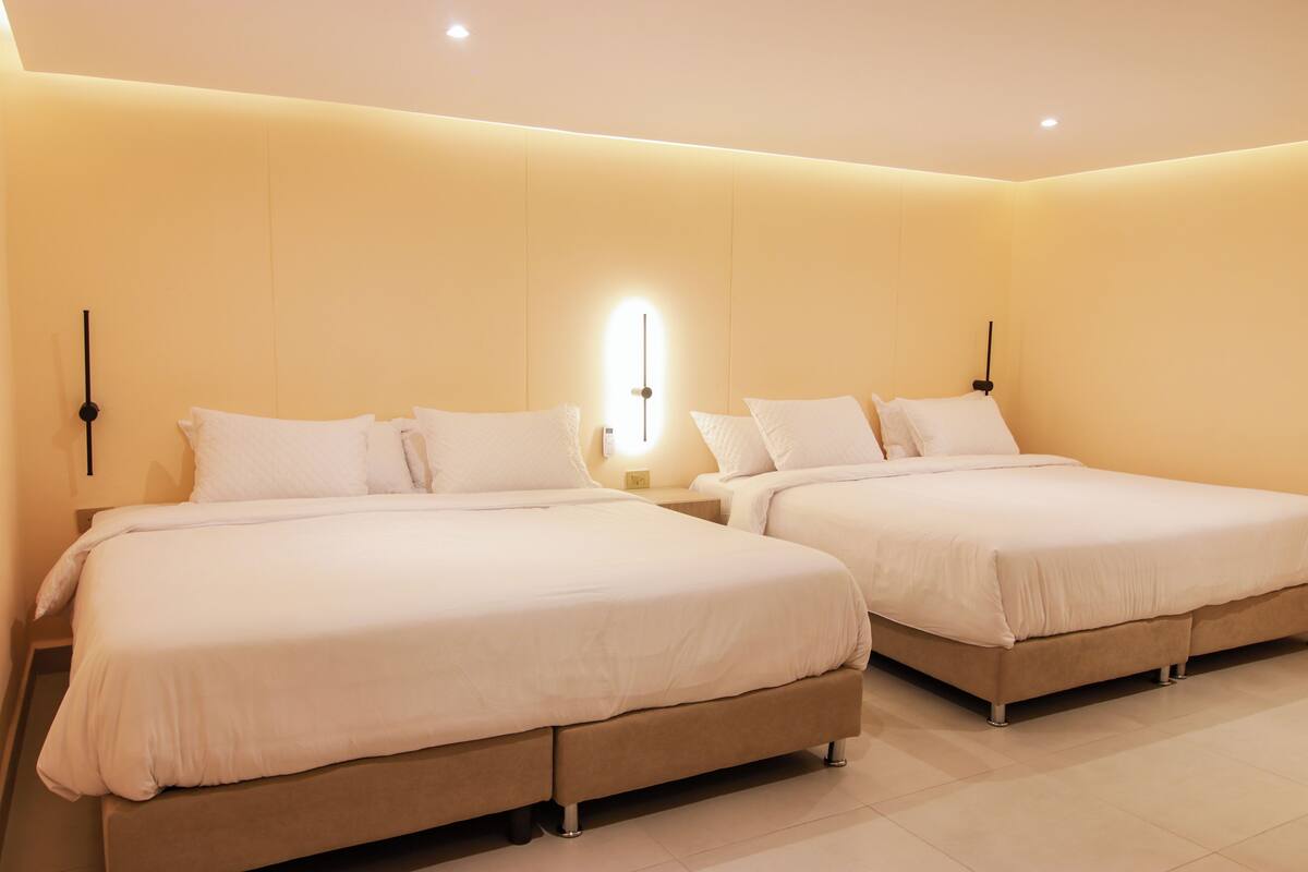 A hotel room with two beds, each with white bedding and a nightstand.