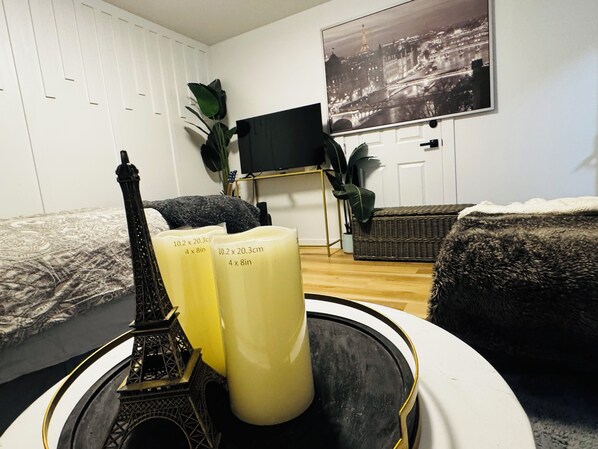 A room with a bed, a small Eiffel Tower model, two candles, a television, and a cityscape painting on the wall.