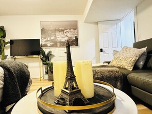 A living room with a model of the Eiffel Tower on a tray, a television, a plant, and a couch with pillows.