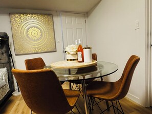 A dining area with a glass table, four brown chairs, a white vase with a rose, and two bottles of wine.
