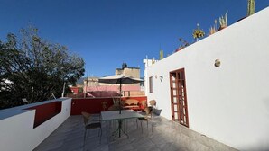 Une terrasse sur le toit avec une table et des chaises, un mur rouge et blanc, et un ciel bleu dégagé.