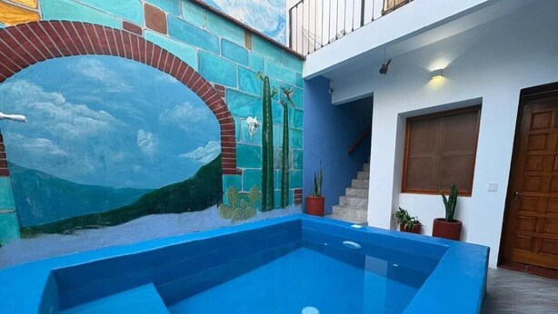 Une piscine aux parois bleues, une fresque représentant un paysage sur le mur adjacent, et un escalier menant à une porte en bois.