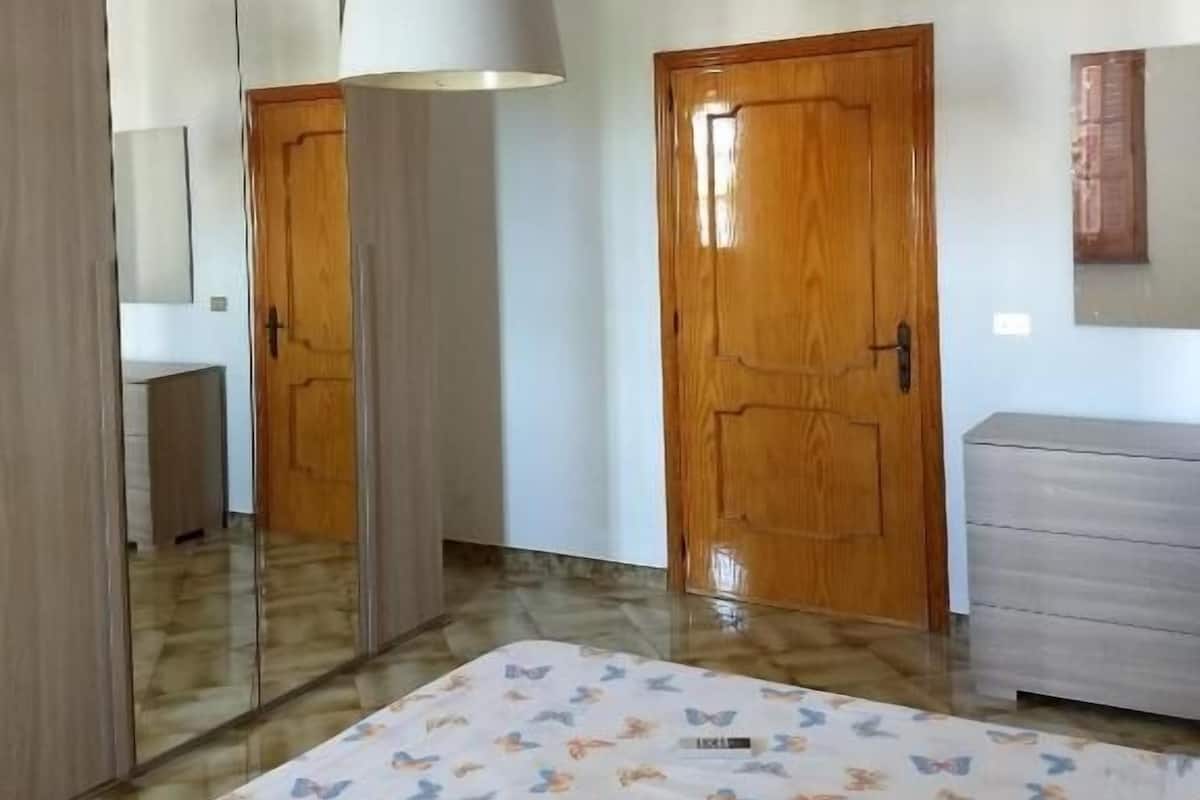 Ein Schlafzimmer mit einem Bett, einer Holztür, einem Spiegel und einer Pendelleuchte.