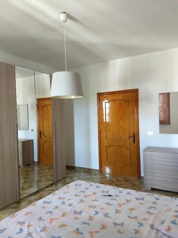 A bedroom with a bed, a wooden door, a mirror, and a hanging light fixture. - Salento Relax Natasha Room (Collepasso)