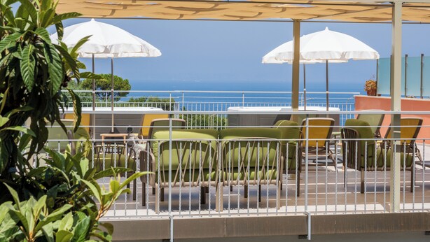 Une terrasse avec des places assises à l’extérieur, des parasols blancs et une vue sur l’océan.