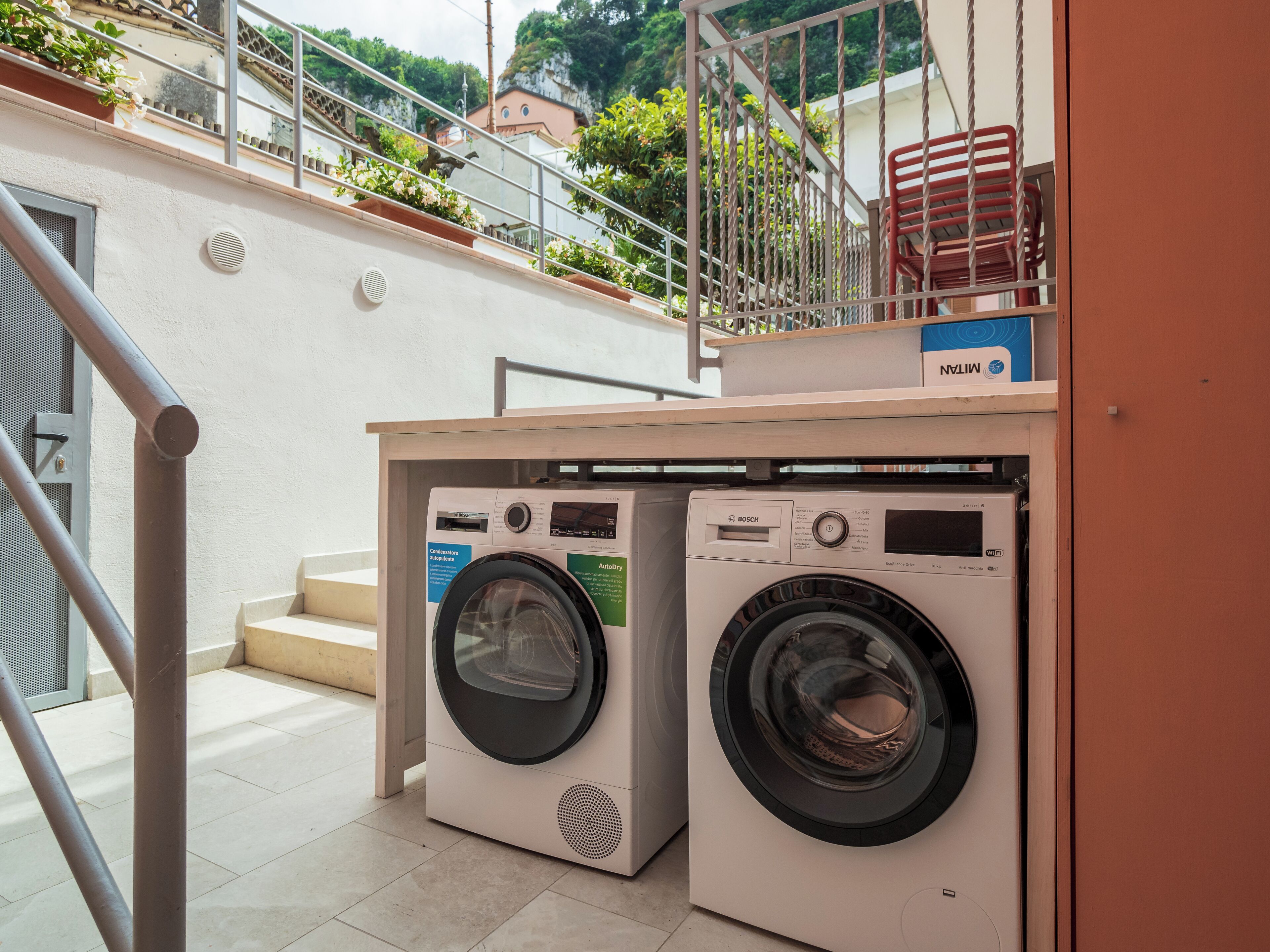 Two Bosch washing machines in a laundry area with a staircase leading to a balcony.