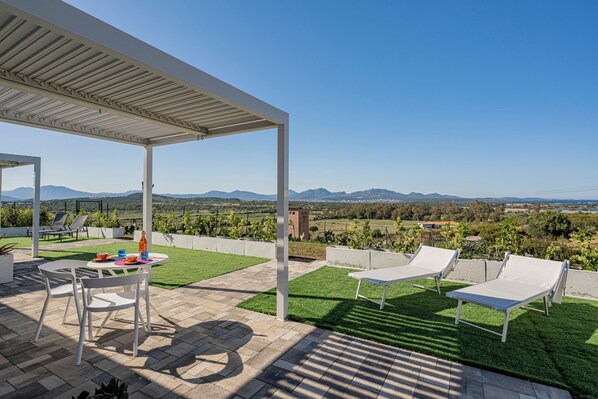 A patio with a table and chairs, a covered area, and a view of the landscape.