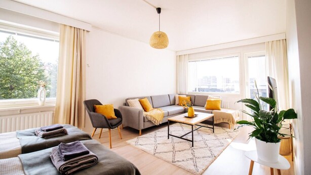 Un salon moderne avec un canapé, des fauteuils, une table basse et une grande fenêtre avec des rideaux.