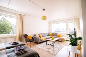 Ein modernes Wohnzimmer mit einer Couch, Sesseln, einem Couchtisch und einem großen Fenster mit Vorhängen.