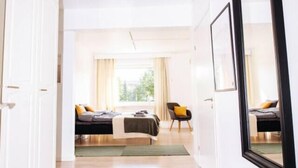 Un couloir menant à une chambre à coucher, où se trouvent un lit, une chaise et une fenêtre avec des rideaux.
