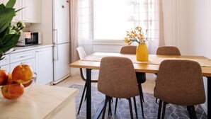 Une cuisine moderne avec des meubles blancs, une table à manger avec quatre chaises, un vase jaune orné de fleurs et un luminaire suspendu.
