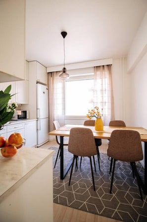 A modern kitchen with white cabinets, a dining table with four chairs, a yellow vase with flowers, and a hanging light fixture. - Come in! `Pirkanportti` In the heart of Tampere (Tampere)