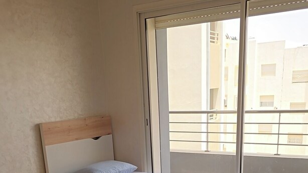 Une chambre d’hôtel avec deux lits, une tête de lit en bois, une table de chevet et une grande fenêtre donnant sur des immeubles.