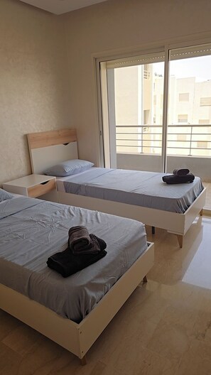 Habitación de hotel con dos camas, cabecero de madera, mesita de noche y una ventana grande con vistas a edificios.