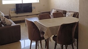 Un salon moderne comprenant un coin repas, un téléviseur à écran plat et une grande fenêtre laissant entrer la lumière naturelle.