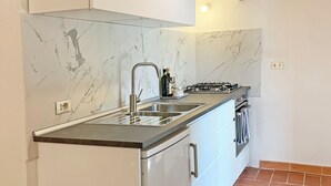 A modern kitchen with white cabinets, a marble backsplash, a stainless steel sink, and a gas stove. - S.M.IL CASTRO a special place at the foot of the castle of Monteriggioni (Monteriggioni)