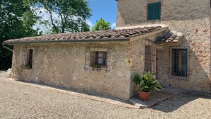 A rustic stone building with a tiled roof, a small balcony with a potted plant, and a gravel driveway. - S.M.IL CASTRO a special place at the foot of the castle of Monteriggioni (Monteriggioni)
