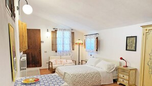 A bedroom with two beds, a dining table with a patterned tablecloth, a radiator, and a lamp. - S.M.IL CASTRO a special place at the foot of the castle of Monteriggioni (Monteriggioni)