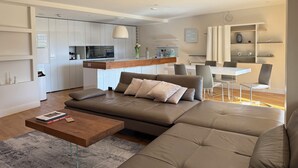 Un salon moderne avec un canapé d’angle marron, une table basse en bois et un coin repas comprenant une table et des chaises blanches.