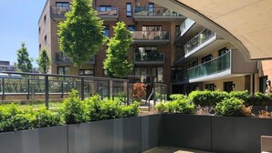 Un espace extérieur moderne doté d’un coin salon incurvé, d’un petit muret agrémenté de verdure et d’un immeuble à plusieurs étages en arrière-plan.
