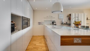 Une cuisine moderne avec des meubles blancs, un plancher en bois et un îlot central agrémenté d’un panier de fruits.